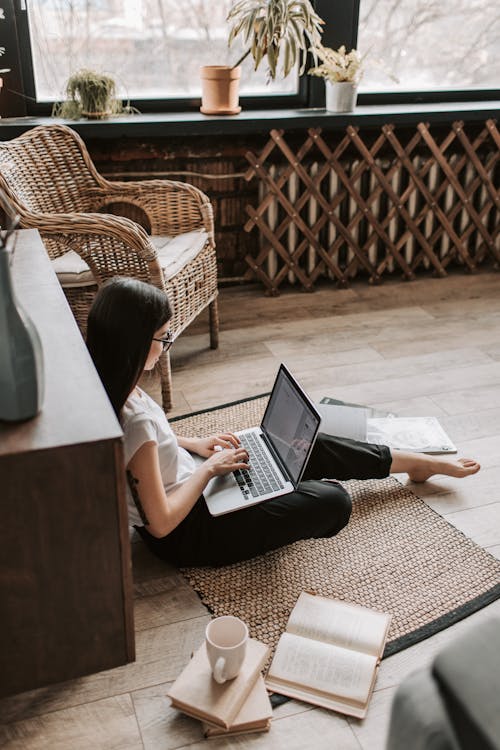 Free Young barefoot woman using laptop on floor near books in stylish living room Stock Photo