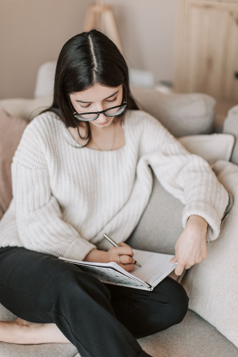 Woman writing in a journal on her sofa at home