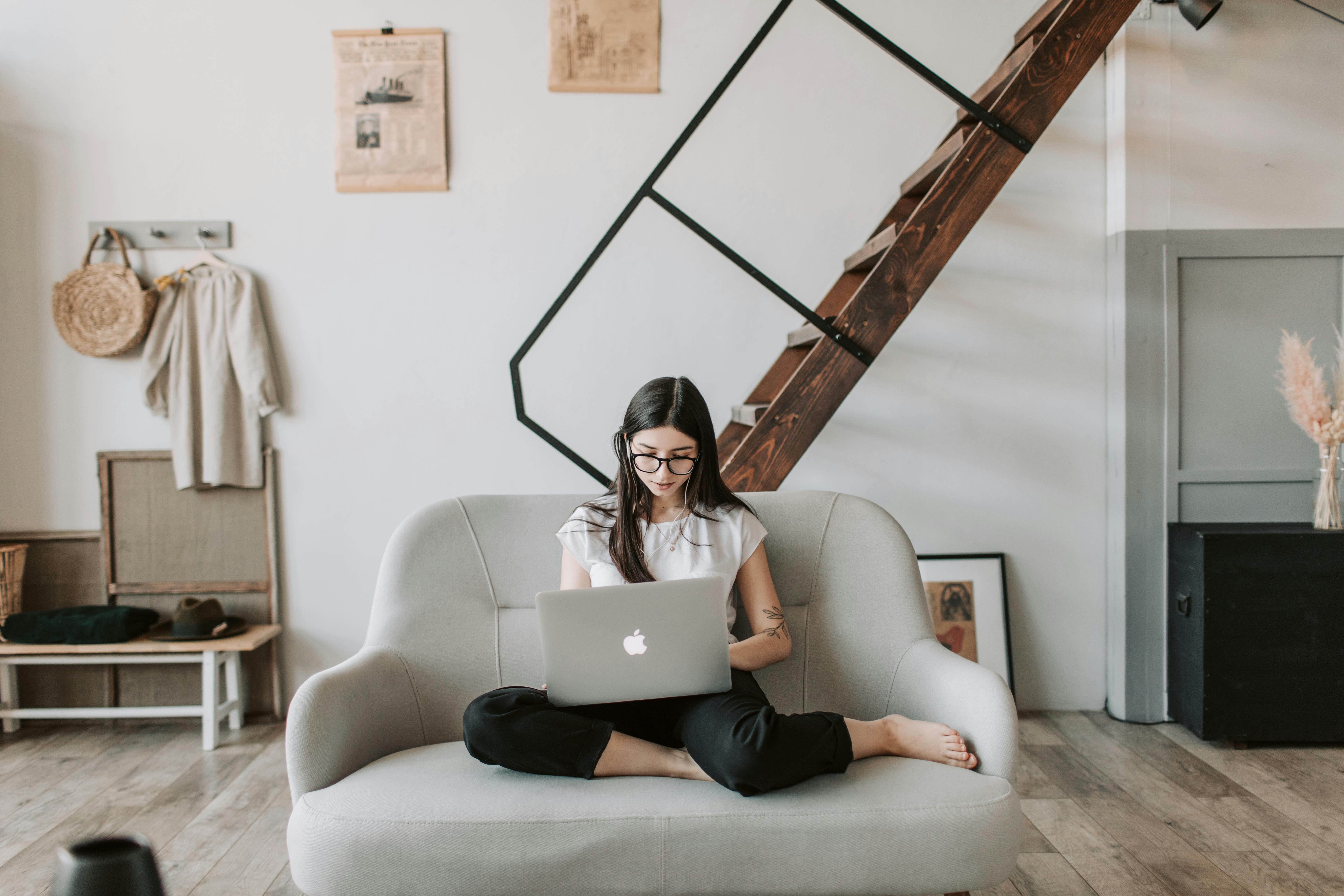 positive young woman using laptop in modern living room with wooden staircase