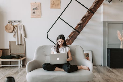 Young woman relaxing at home on a sofa with a laptop, working remotely in a cozy living space.