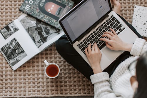 Free Crop young businesswoman using laptop while drinking tea at home Stock Photo