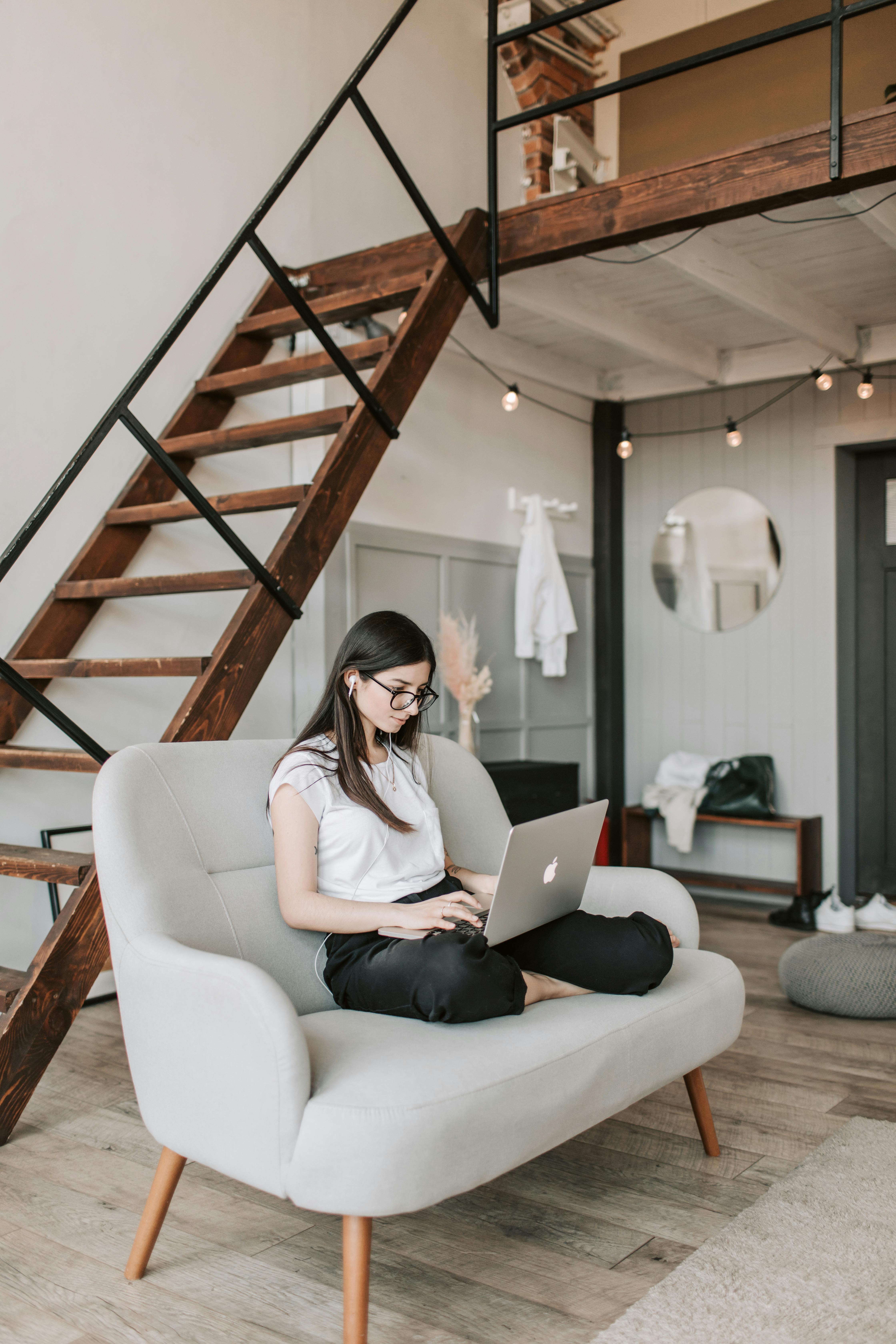 young woman using laptop in modern living room with wooden staircase