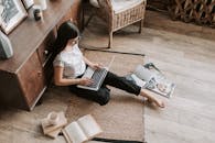 在休闲的家庭工作空间里，一名女性正使用笔记本电脑，周围摆满了书籍和杂志