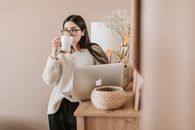 一位年轻女子在舒适的室内，一边喝咖啡一边用笔记本电脑工作
