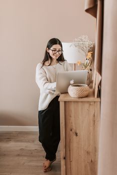 一位妇女穿着休闲服装，在家里用笔记本电脑，展现出轻松的生活方式