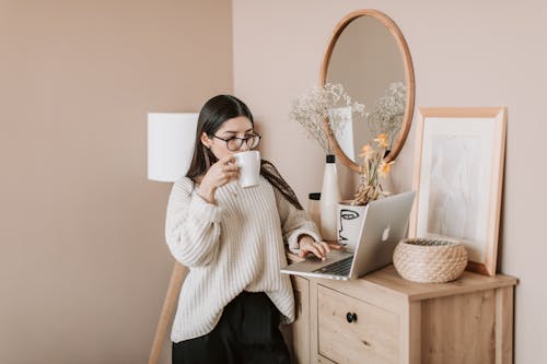 Free Busy female using laptop and drinking hot beverage at home Stock Photo
