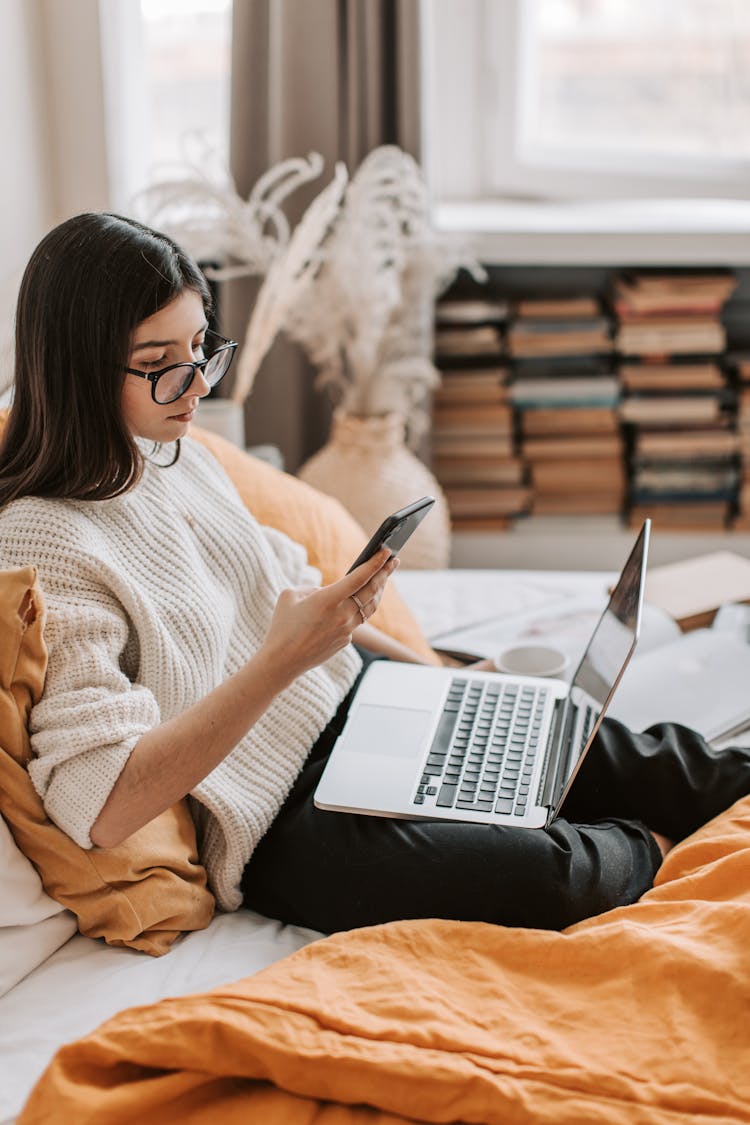 Young Lady Using Laptop And Smartphone On Bed