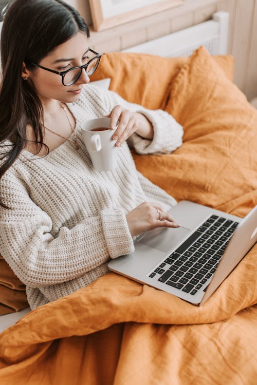 Young woman using laptop and drinking tea on bed