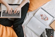 一个女人在舒适的卧室里，周围摆满了书籍和个人物品，正用笔记本电脑工作