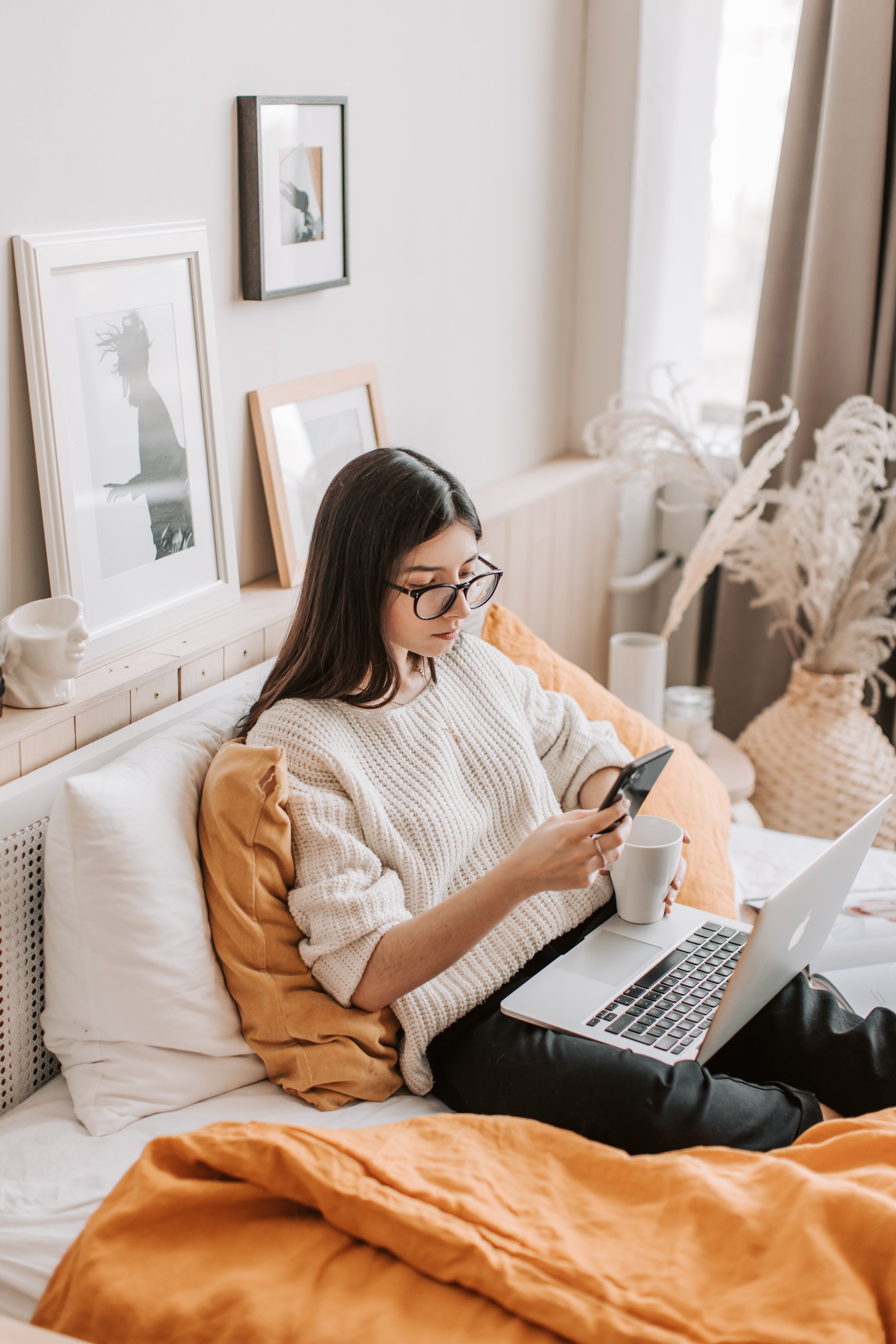 woman with laptop and mug using smartphone on bed