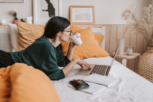 Free Woman using laptop and drinking beverage in bed Stock Photo