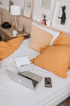 A cozy home workspace setup on a bed with a laptop, smartphone, and decorative accents.