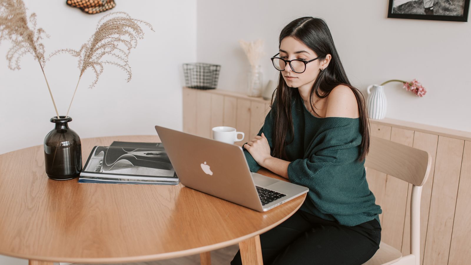 Mother working on a laptop at a cozy home desk with a notebook and coffee