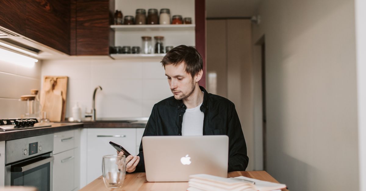 A person at a kitchen table with a laptop and notebook, looking thoughtful, not stressed