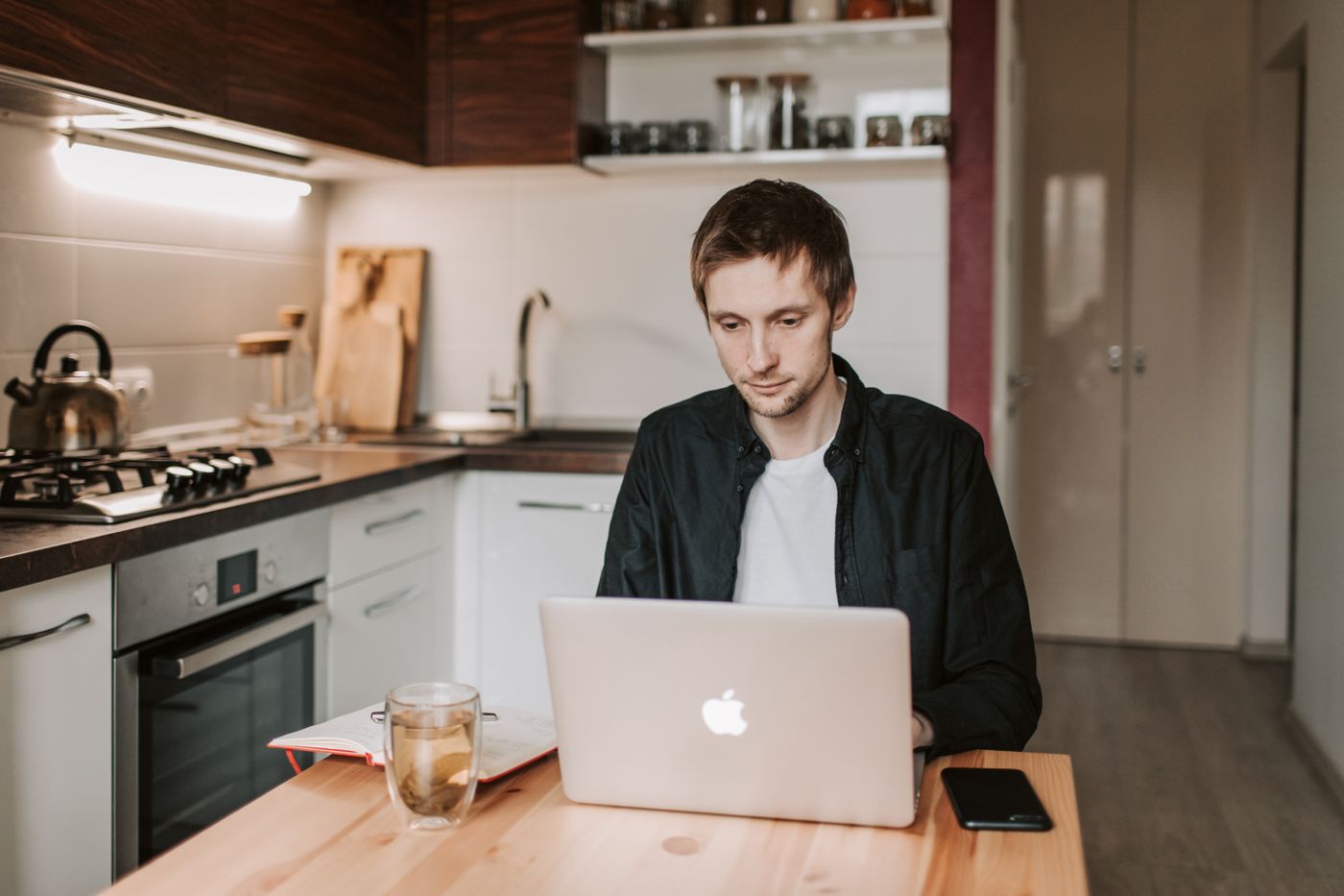 Junger Mann arbeitet konzentriert am Laptop in einer gemütlichen Küche