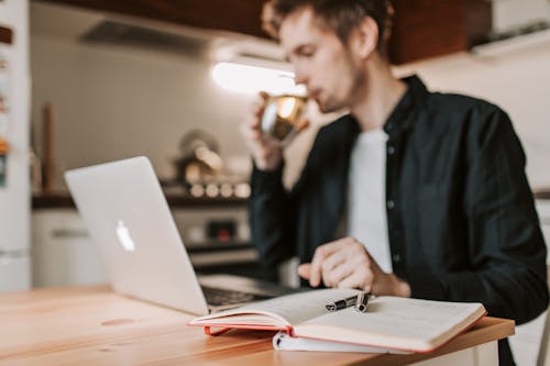 Crop male freelancer drinking water while watching laptop in kitchen