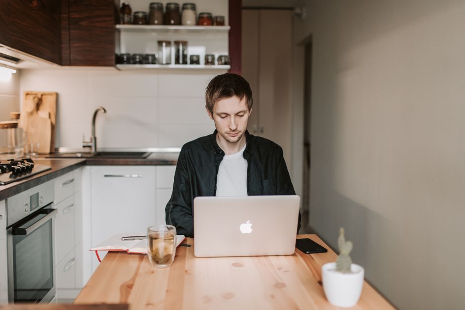 Young adult working remotely in a modern kitchen with laptop.