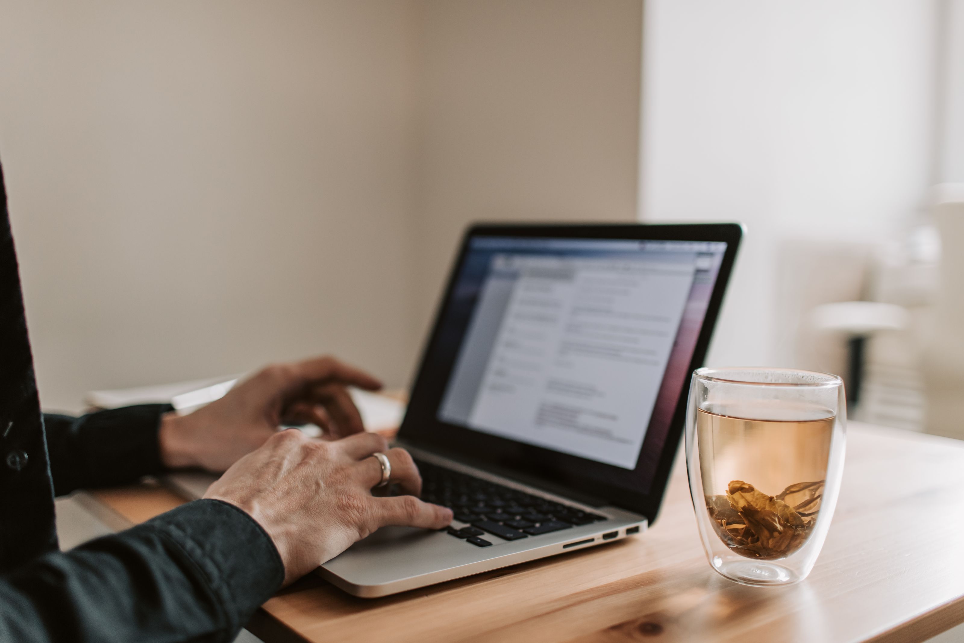 Adult working on laptop with a cup of tea, showcasing remote work lifestyle.