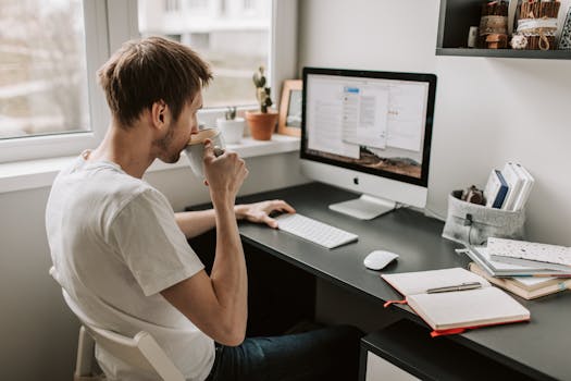 Man sipping coffee while working remotely on a computer at home. Relaxed atmosphere with digital device.