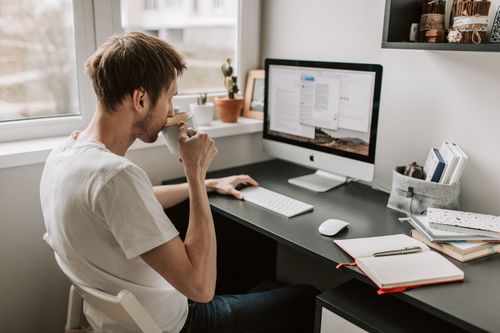 Free Man sipping coffee while working remotely on a computer at home. Relaxed atmosphere with digital device. Stock Photo