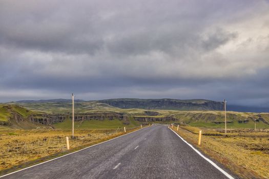 Empty road leading through Iceland's remote and dramatic landscape under a cloudy sky.