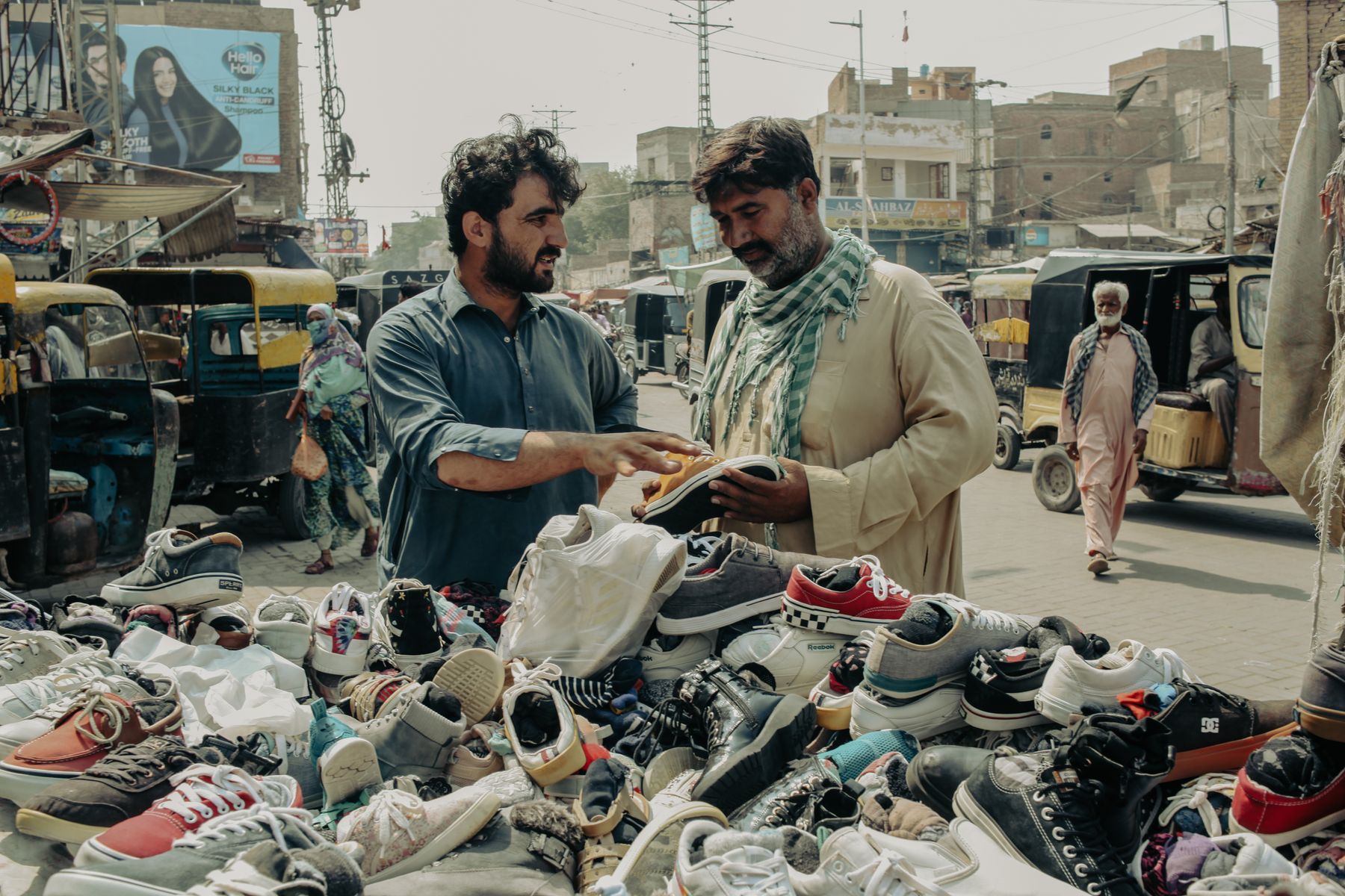 Two men engage in bargaining over secondhand shoes at a bustling street market in Hyderabad, Sindh, Pakistan.