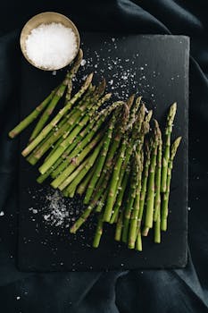 Top view of fresh green asparagus sprinkled with coarse salt on a slate board, highlighting its freshness and flavor.