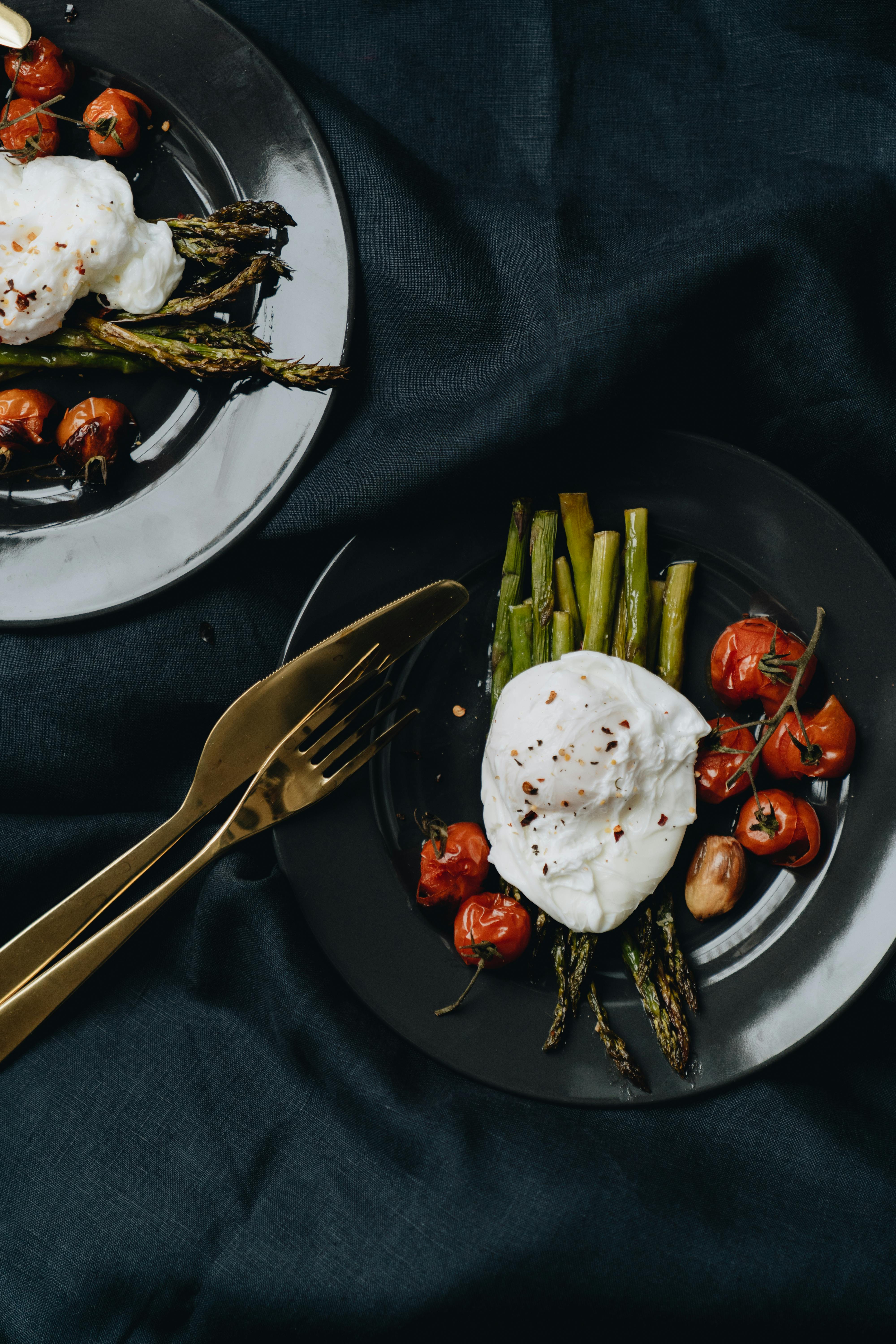 A stylish flatlay of asparagus, cherry tomatoes, and poached eggs on dark plates, perfect for food enthusiasts.