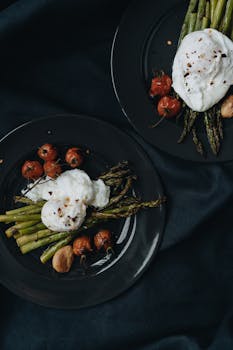 A stylish arrangement of asparagus, cherry tomatoes, and burrata on a plate.