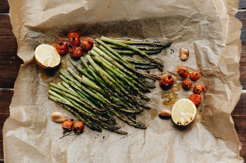 Free Delicious roasted asparagus with cherry tomatoes and lemon on parchment paper, perfect for a healthy meal. Stock Photo