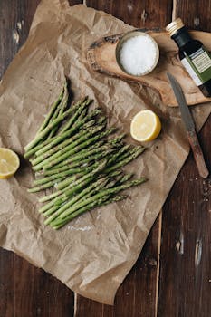 Top view of fresh asparagus with lemon, salt, and olive oil on rustic paper.
