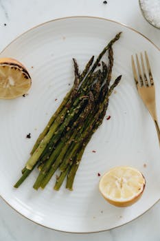 Delicious roasted asparagus served on a ceramic plate with grilled lemon and fork for a healthy meal.