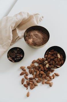 Flat lay of almonds, cocoa powder, and chocolate chips on white surface with cloth backdrop.