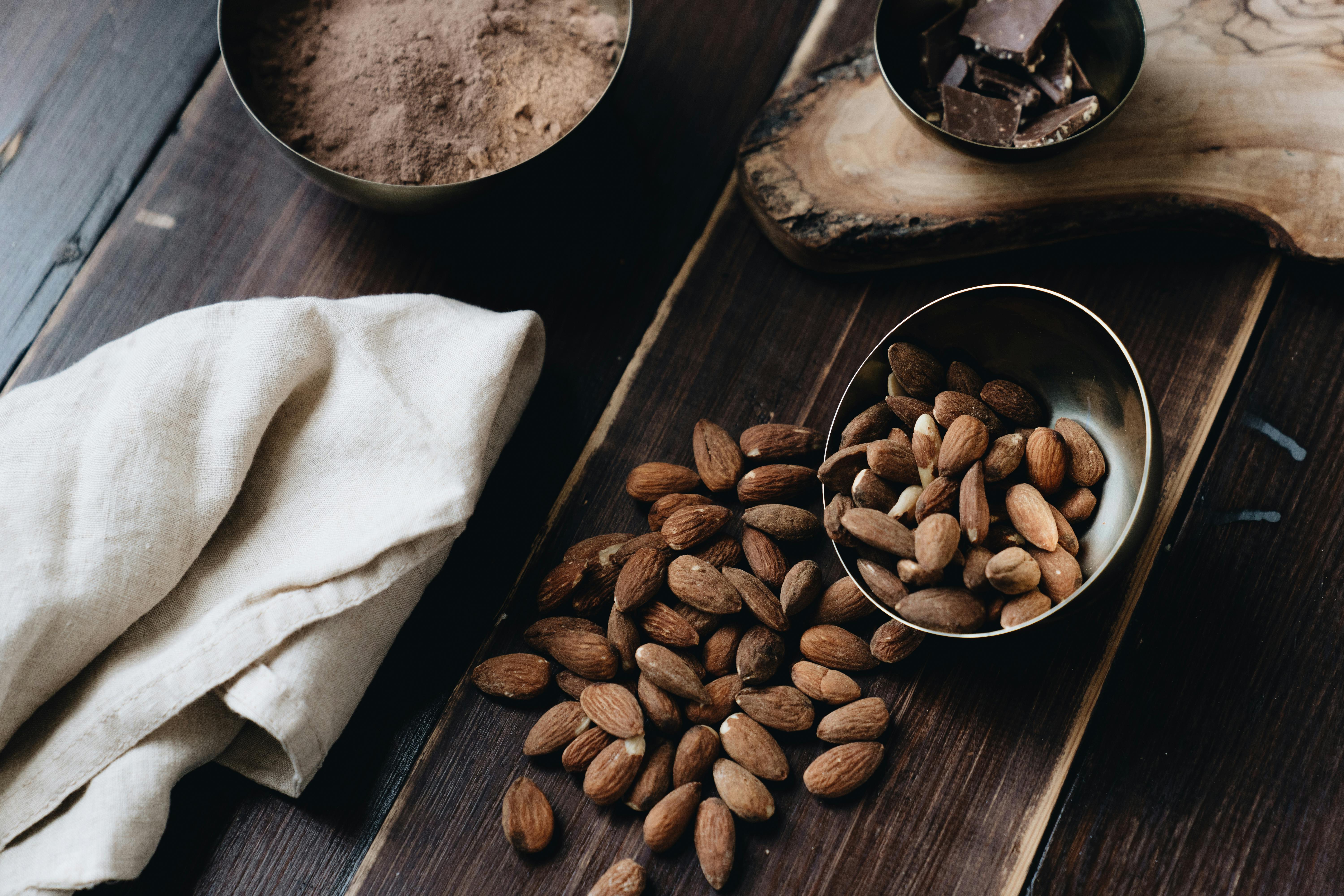 A still life composition with almonds, chocolate, and cacao powder on a wooden surface, creating a warm and delicious atmosphere.