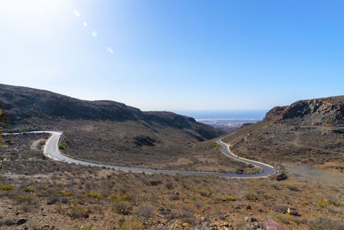 Gray Asphalt Road Between Green Grass Covered Mountains Under Blue Sky