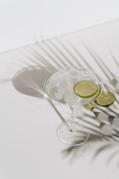 Free A chilled lime cocktail with ice on a white table, casting dramatic shadows from palm leaves. Stock Photo