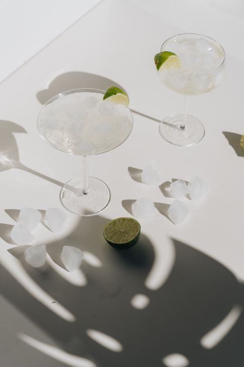Free Two margarita glasses with ice and lime wedges casting shadows, a refreshing summer drink setup. Stock Photo