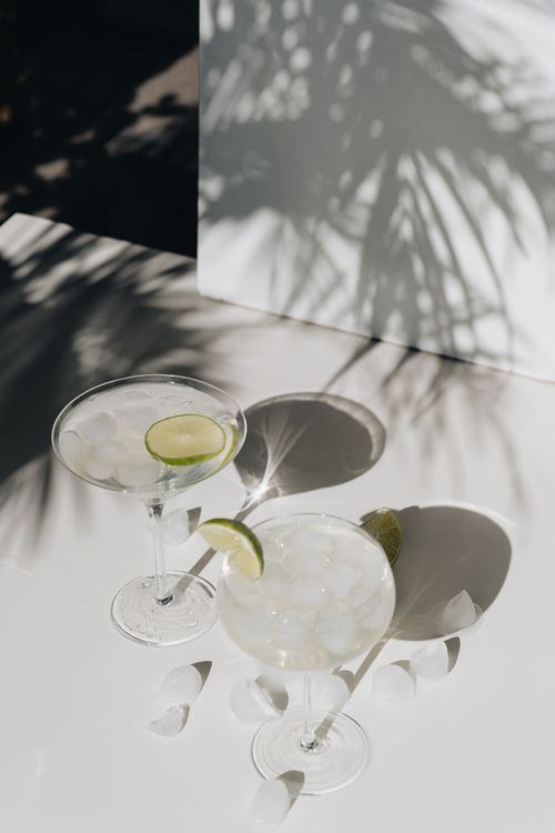 Free Two lime cocktails with ice, casting shadows in bright sunlight on a white surface. Stock Photo