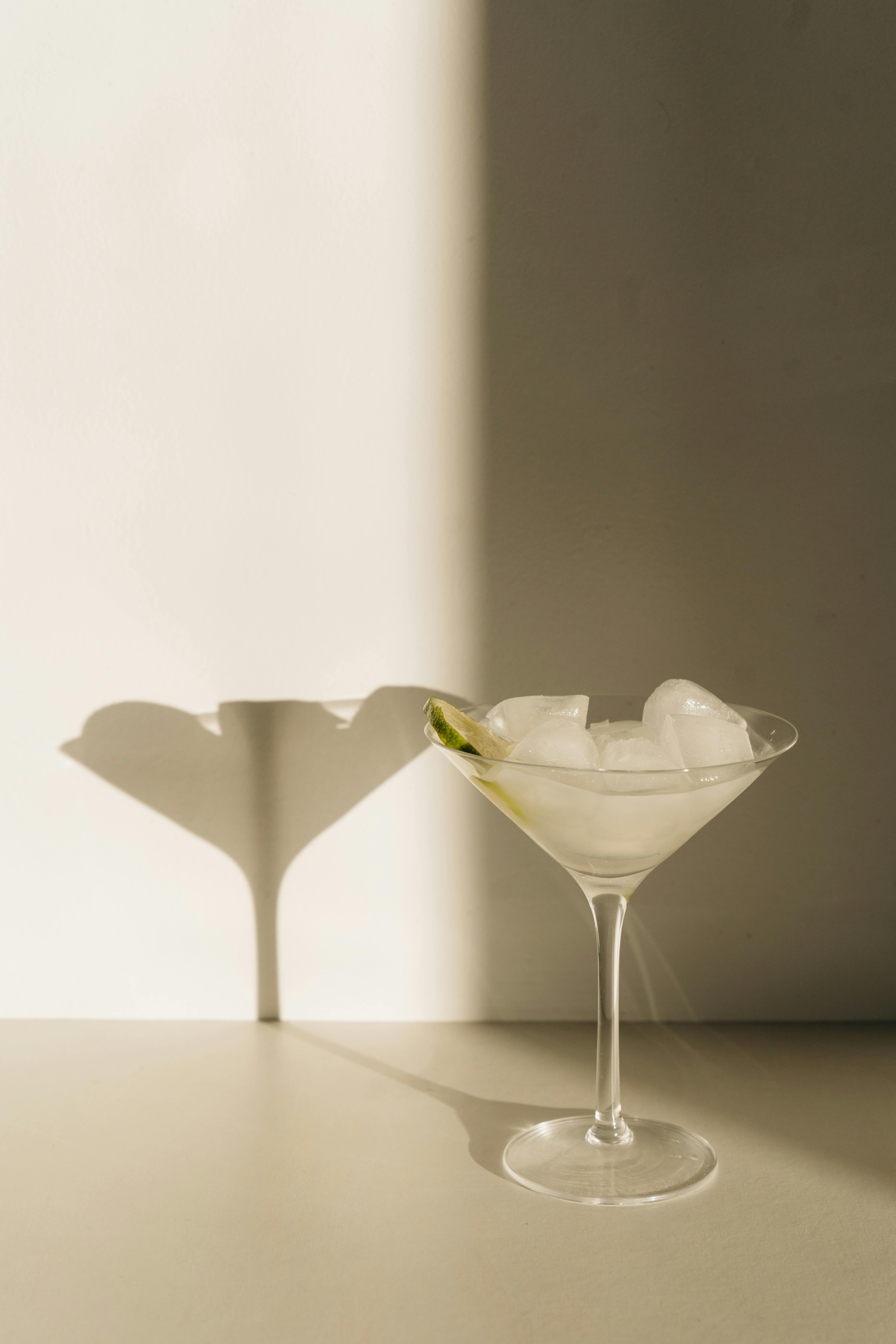 Minimalist photo of a martini glass with lime and ice casting a shadow.