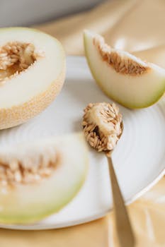 Close up of fresh cantaloupe slices and seeds on a ceramic plate.