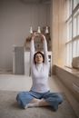 一位女士坐在瑜伽垫上，在宁静的室内环境中向上伸展手臂
