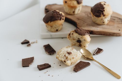 Free Chocolate chip muffins with chunks of chocolate and a gold spoon on a white surface. Stock Photo