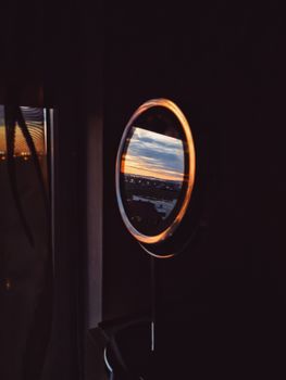 Round mirror with illuminated lamps placed on table in dark room and reflecting street during sunset