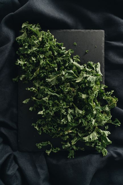 Dark and moody image of freshly chopped kale leaves on a black slate background.