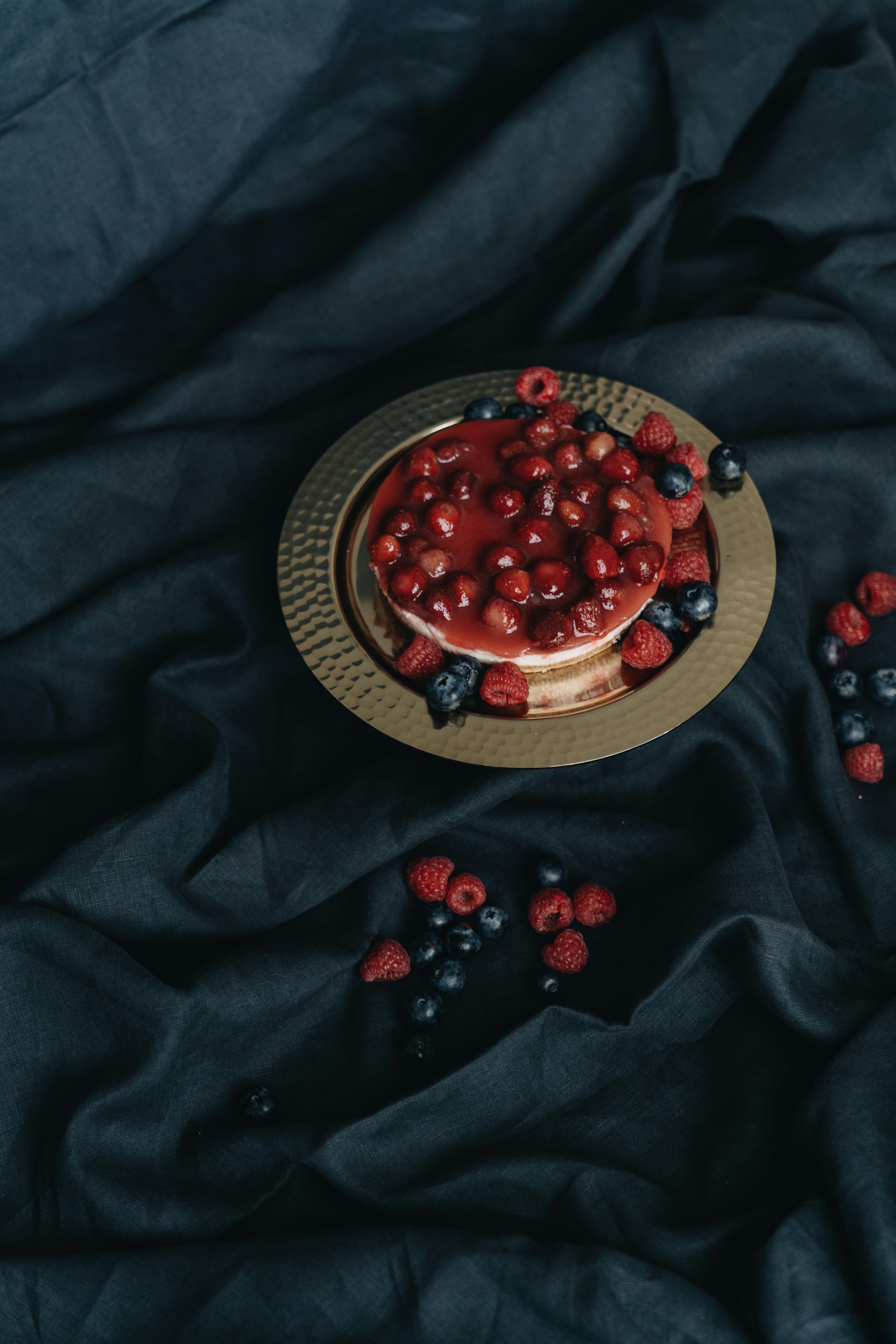 Beautiful berry tart with blueberries and raspberries on a gold plate against a dark fabric backdrop, creating a luxurious feel.