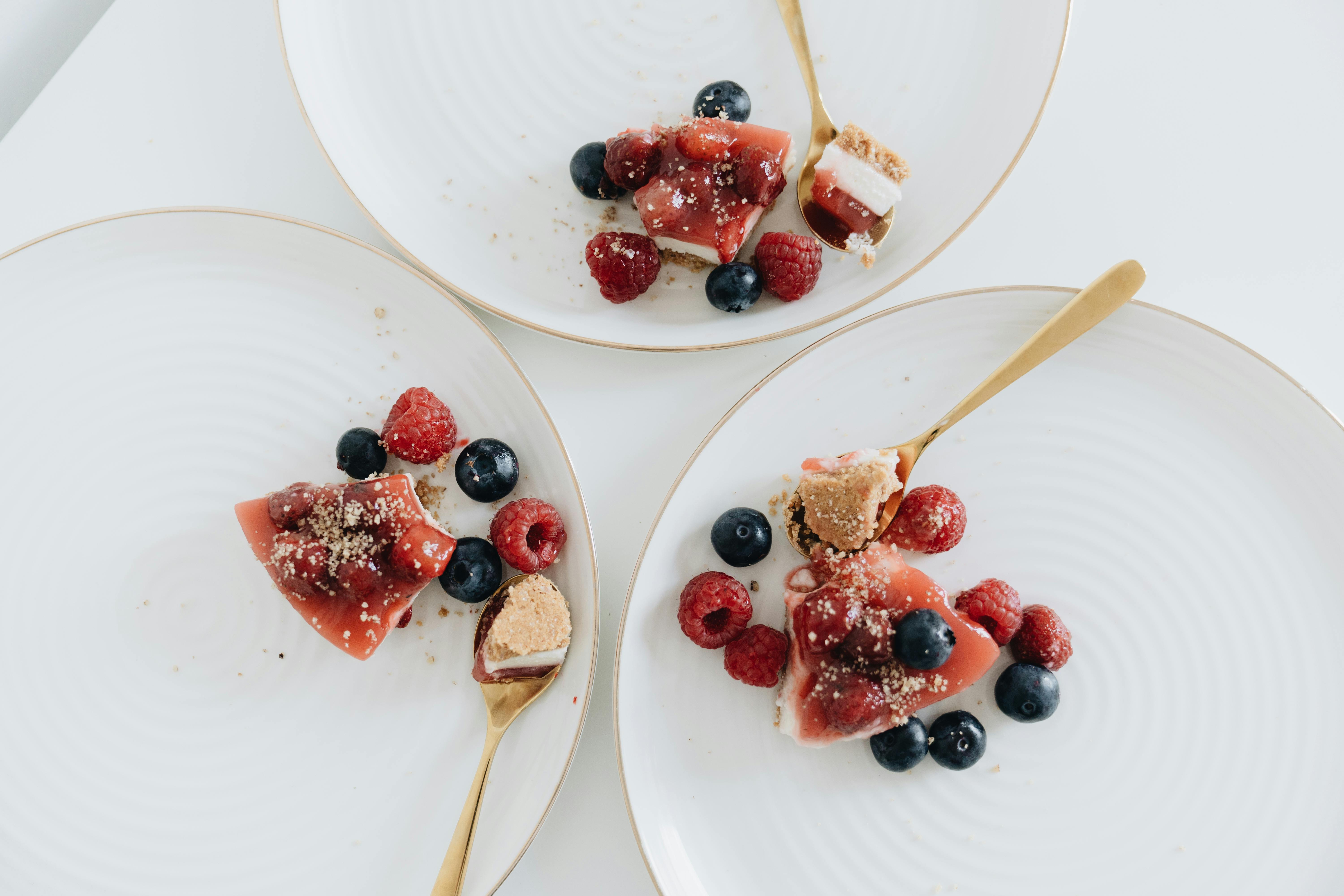 A close-up image of luscious berry-topped cheesecake slices with raspberries and blueberries on elegant white plates.