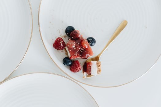 Close-up of a cheesecake slice with fresh raspberries and blueberries on a white plate.