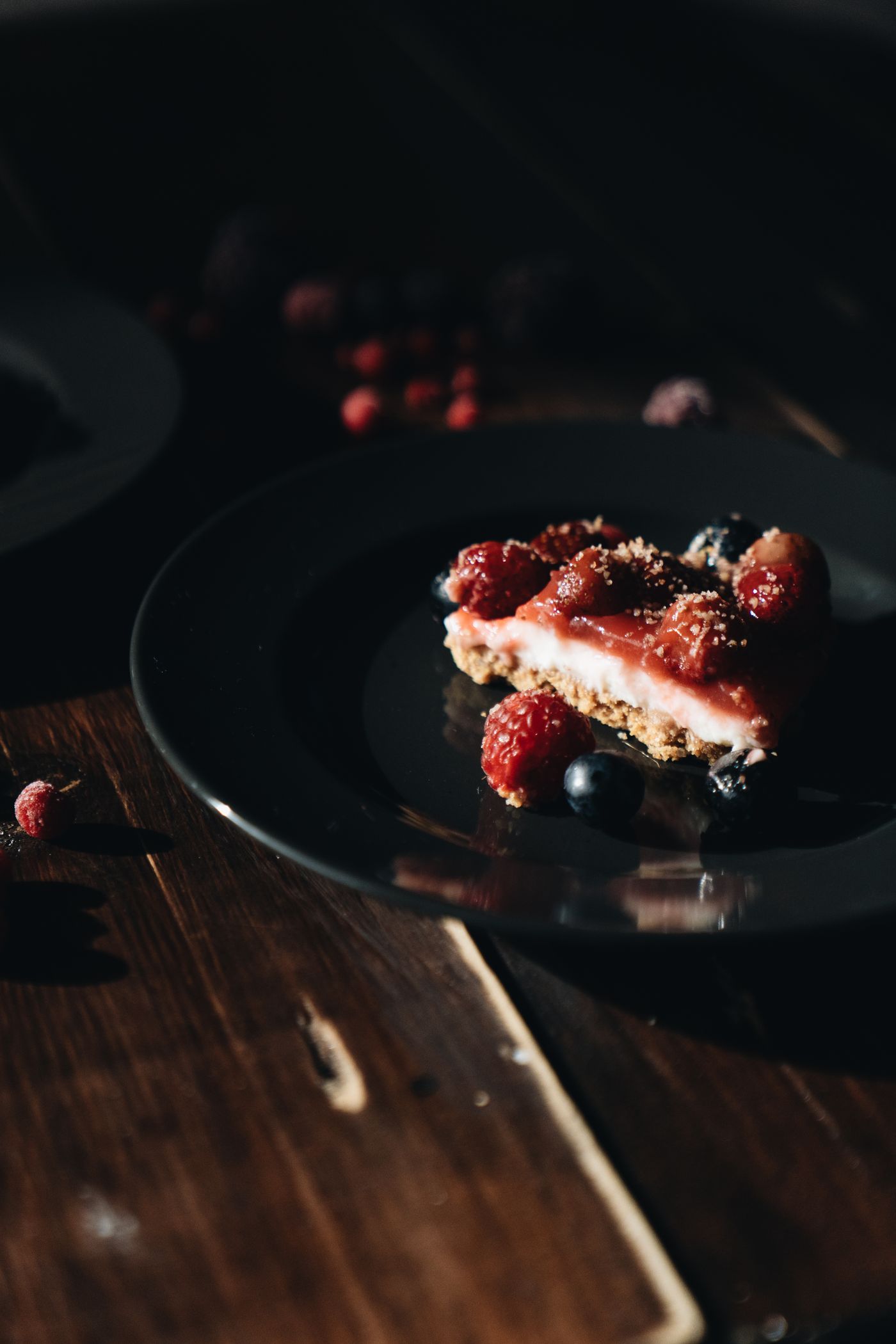 Fetta di cheesecake con frutti di bosco servita su un piatto nero