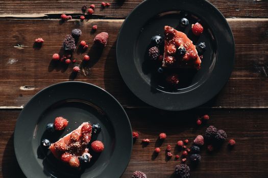 Enticing overhead view of berry-topped cheesecake slices on black plates, highlighting dessert elegance.
