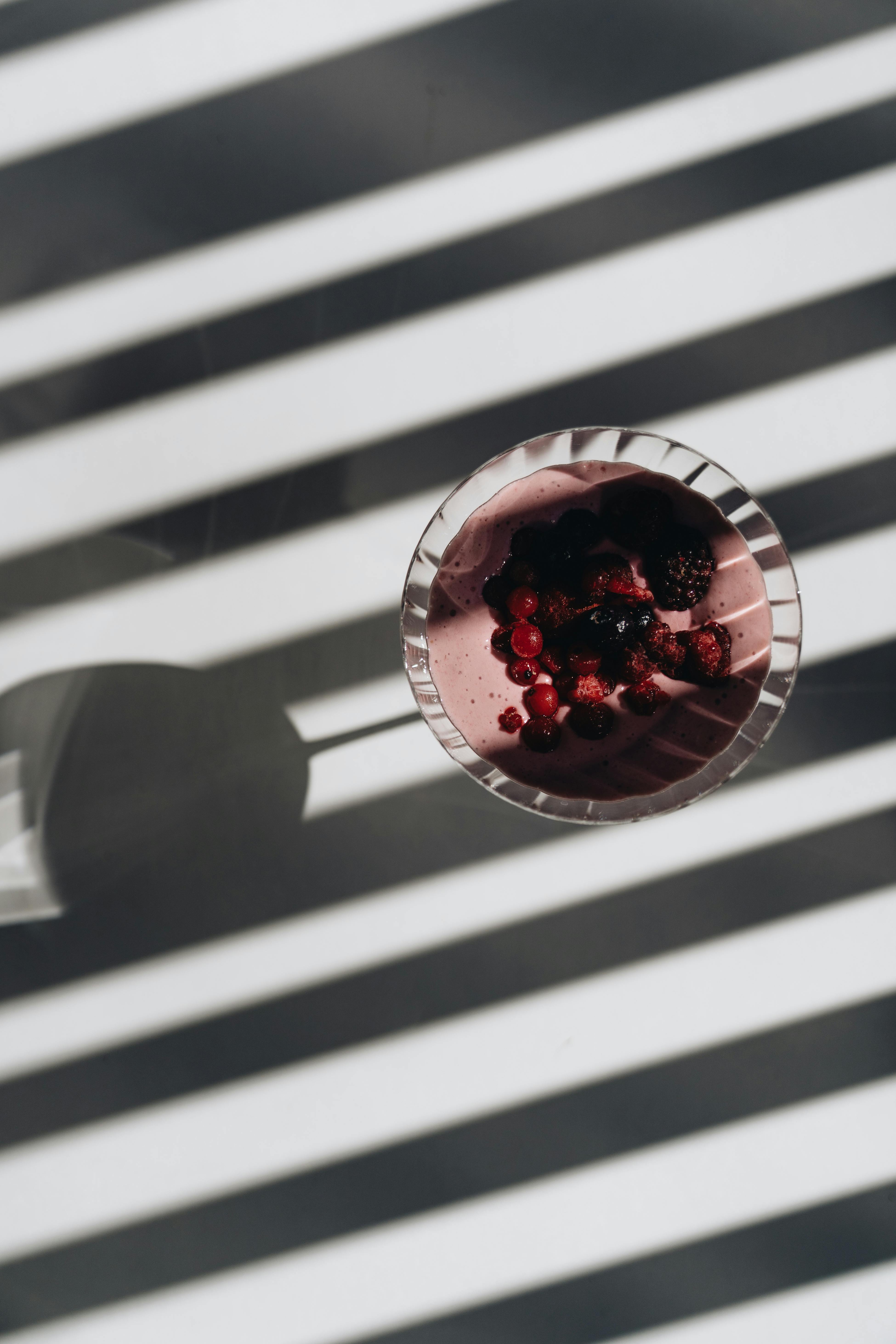 Top view of a berry smoothie in glass with creative stripe shadows, ideal for healthy eating concepts.
